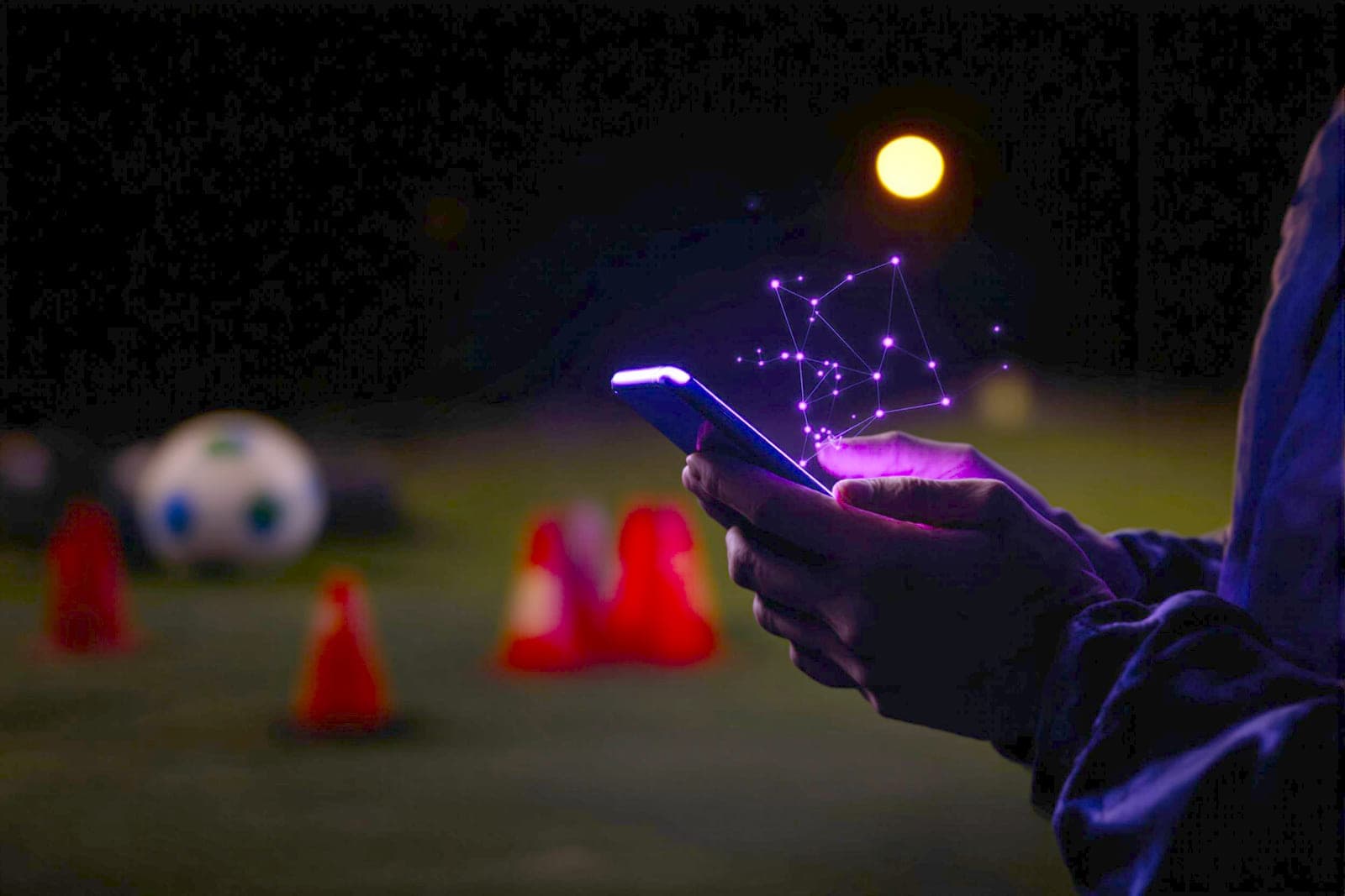 A coach at a dark touchline, a phone screen the only light on their hands.